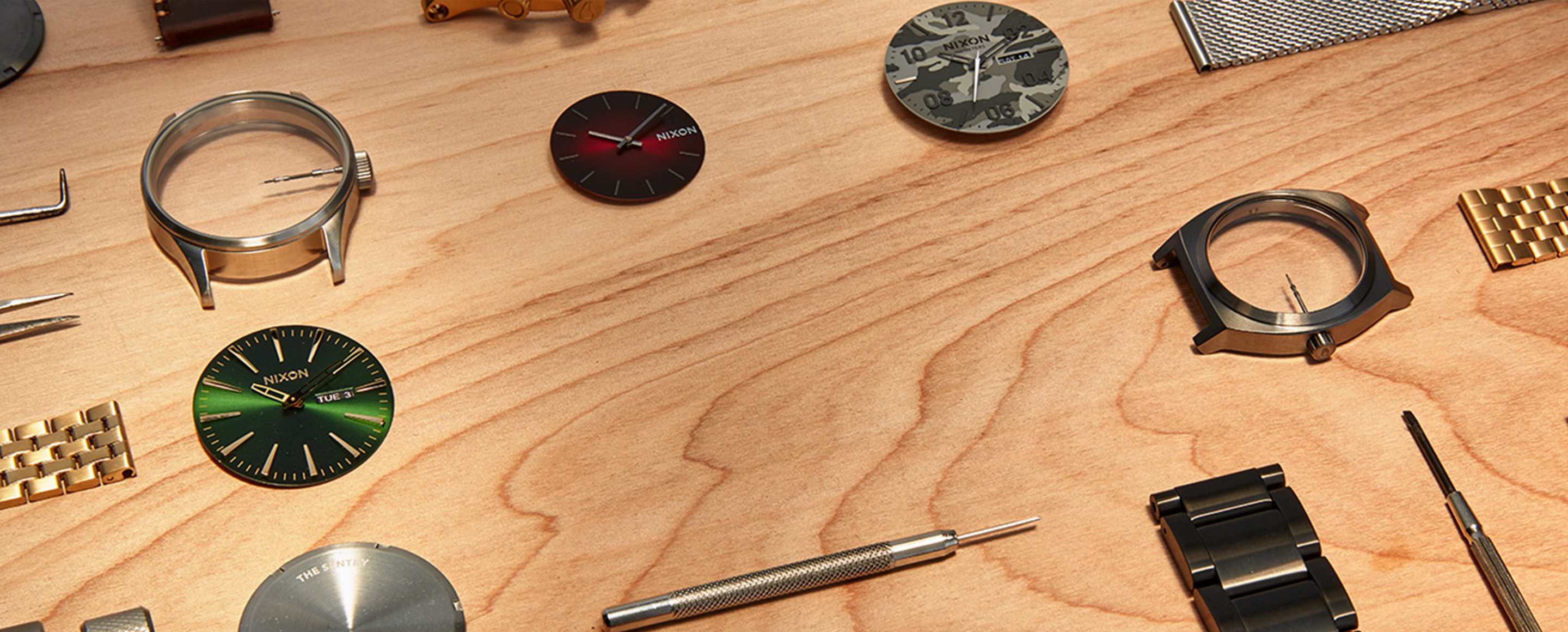 A selection of Nixon custom watch parts are spread out on a wooden table.
